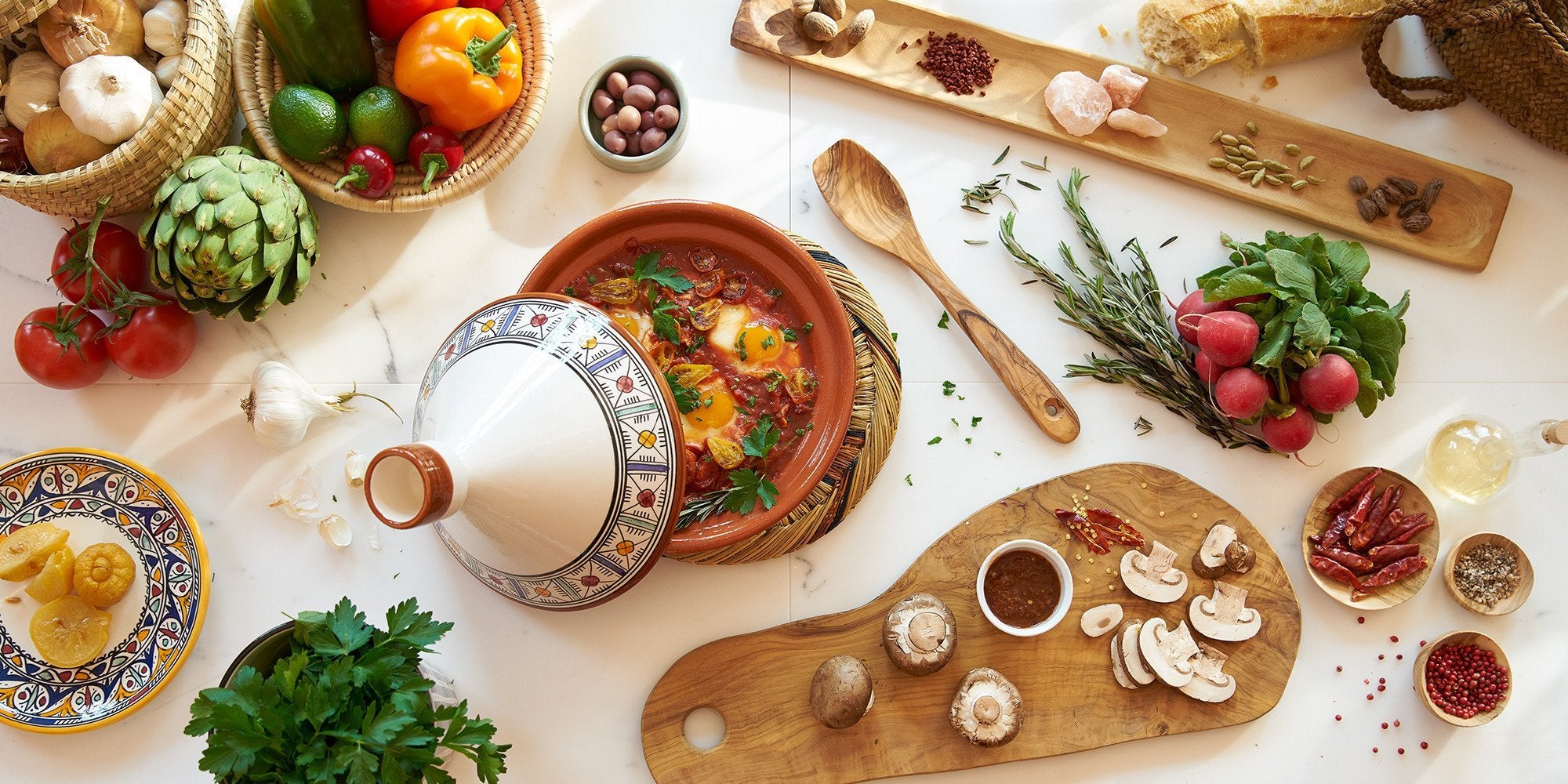 Cooking Tagines with various cutlery, spices, and food - on a white table.